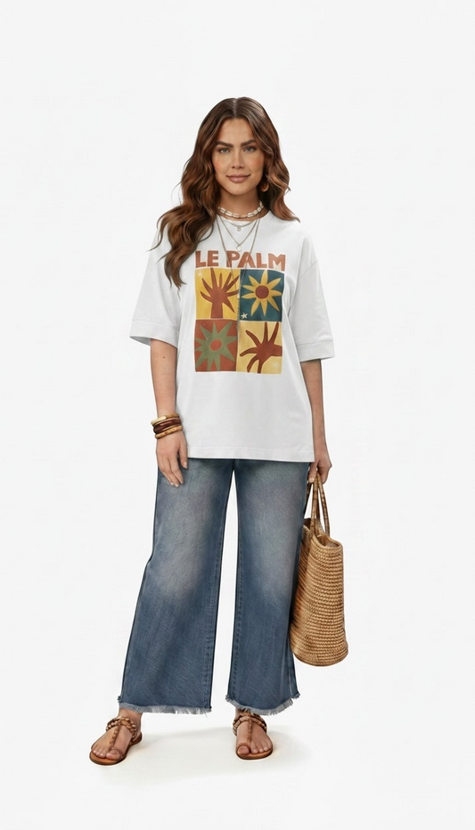 Talla | طلةّ white oversized cotton t-shirt with Le Palm graphic print worn by a woman with wide-leg jeans and straw bag