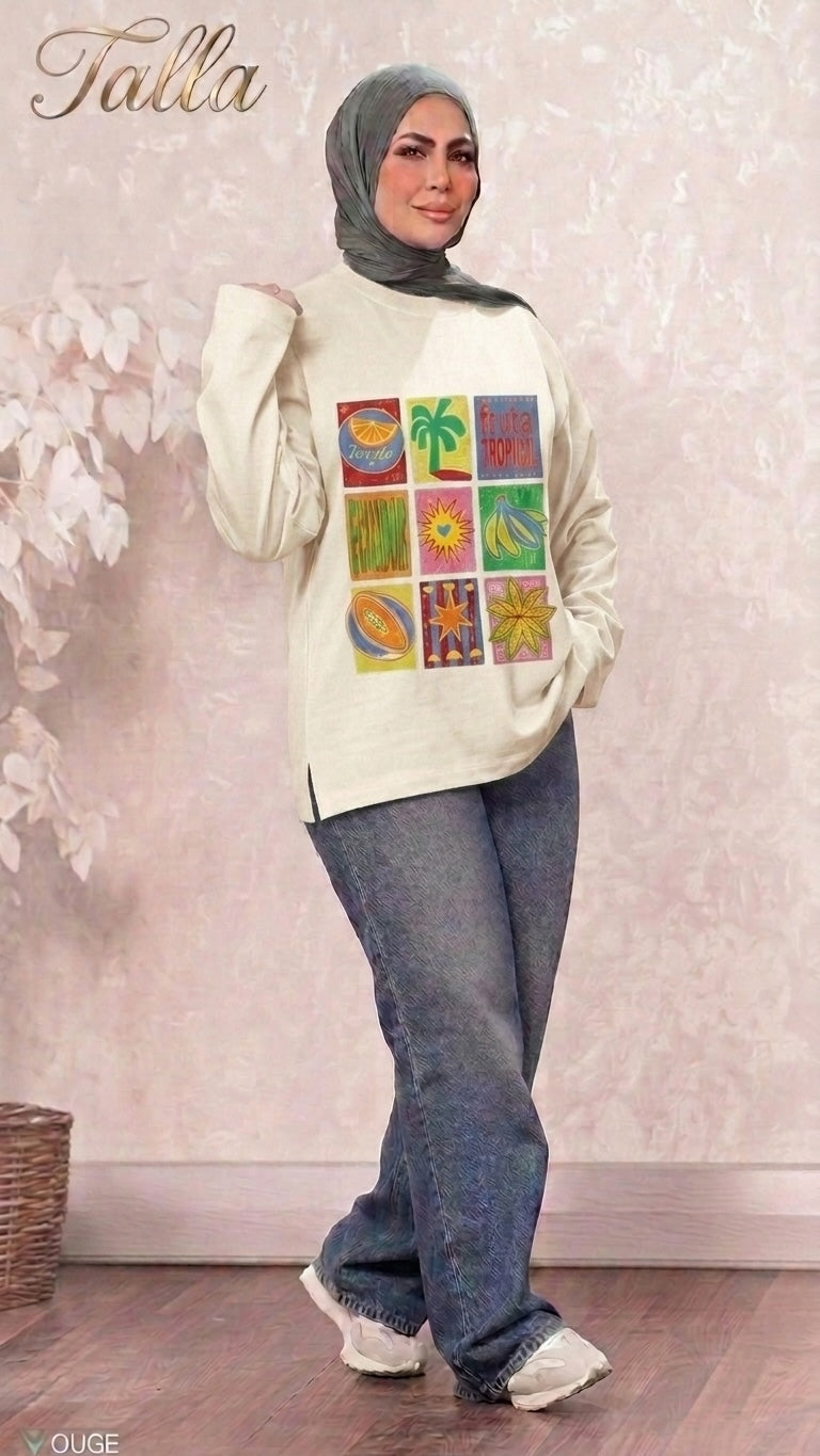 Talla | طلةّ cream long sleeve sweatshirt with tropical fruit grid graphic print, worn with jeans and a grey hijab.