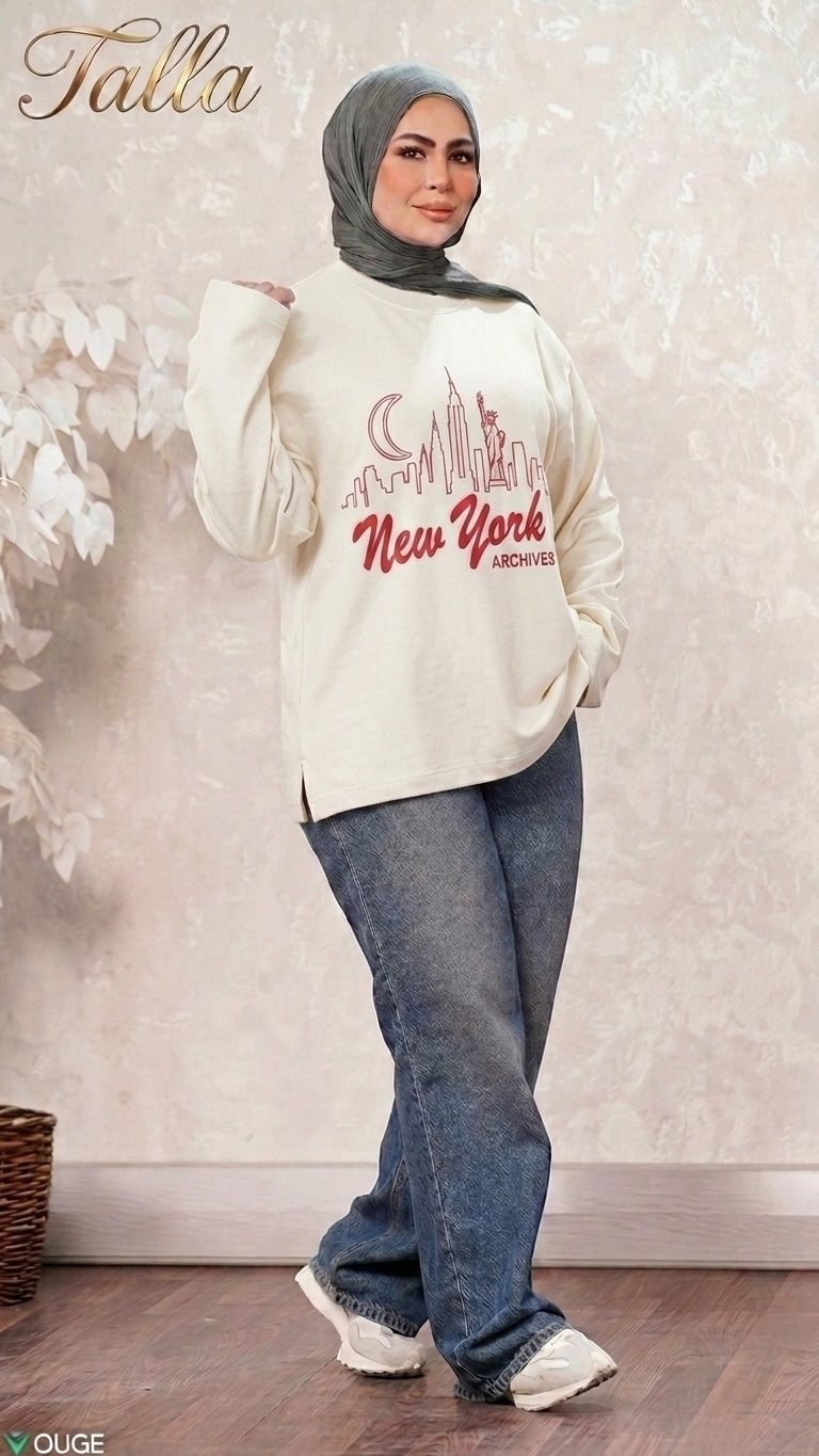 Talla | طلةّ cream sweatshirt with New York skyline graphic, worn by a model in a hijab and blue jeans.