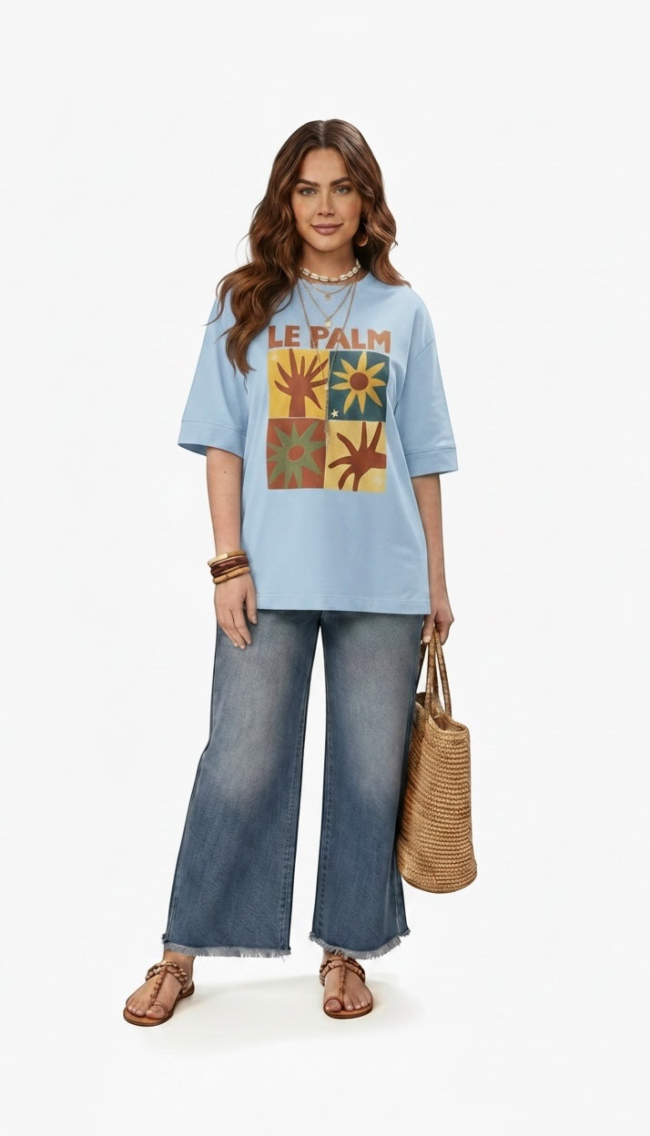 Talla | طلةّ light blue oversized cotton t-shirt with Le Palm graphic print, worn by a model with wide-leg jeans.