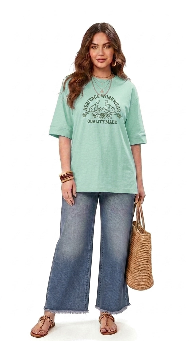Talla | طلةّ oversized mint green graphic t-shirt with elbow-length sleeves worn with wide-leg jeans and a straw bag.