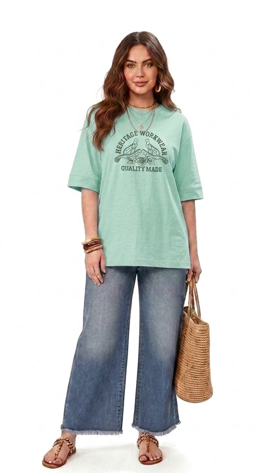 Talla | طلةّ oversized mint green graphic t-shirt with elbow-length sleeves worn with wide-leg jeans and a straw bag.