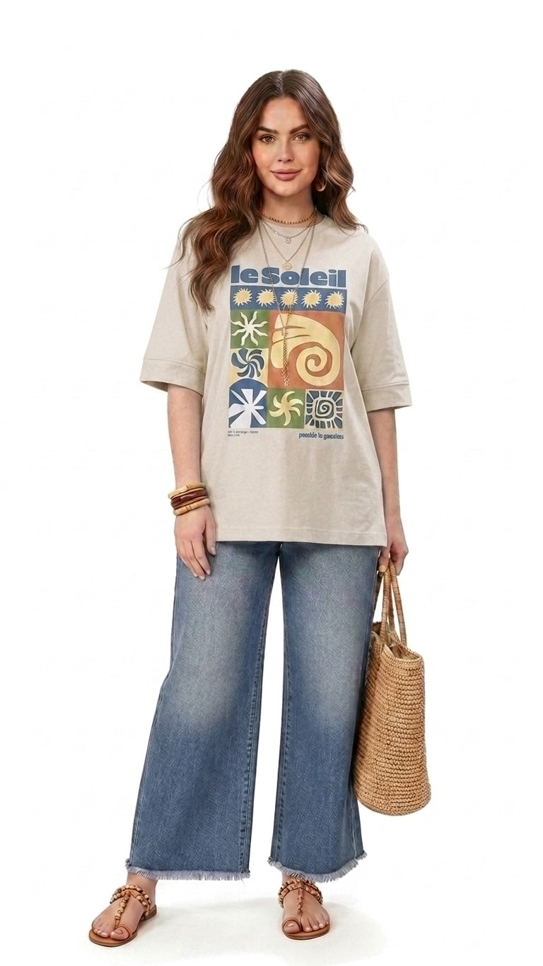 Talla | طلةّ oversized beige cotton t-shirt with a colorful sun-inspired graphic print worn by a model with jeans.