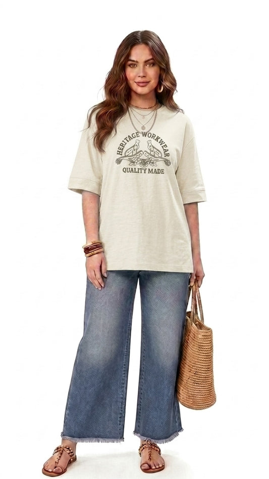 Talla | طلةّ oversized beige cotton t-shirt with vintage graphic print, worn by a woman with wide-leg jeans and sandals.