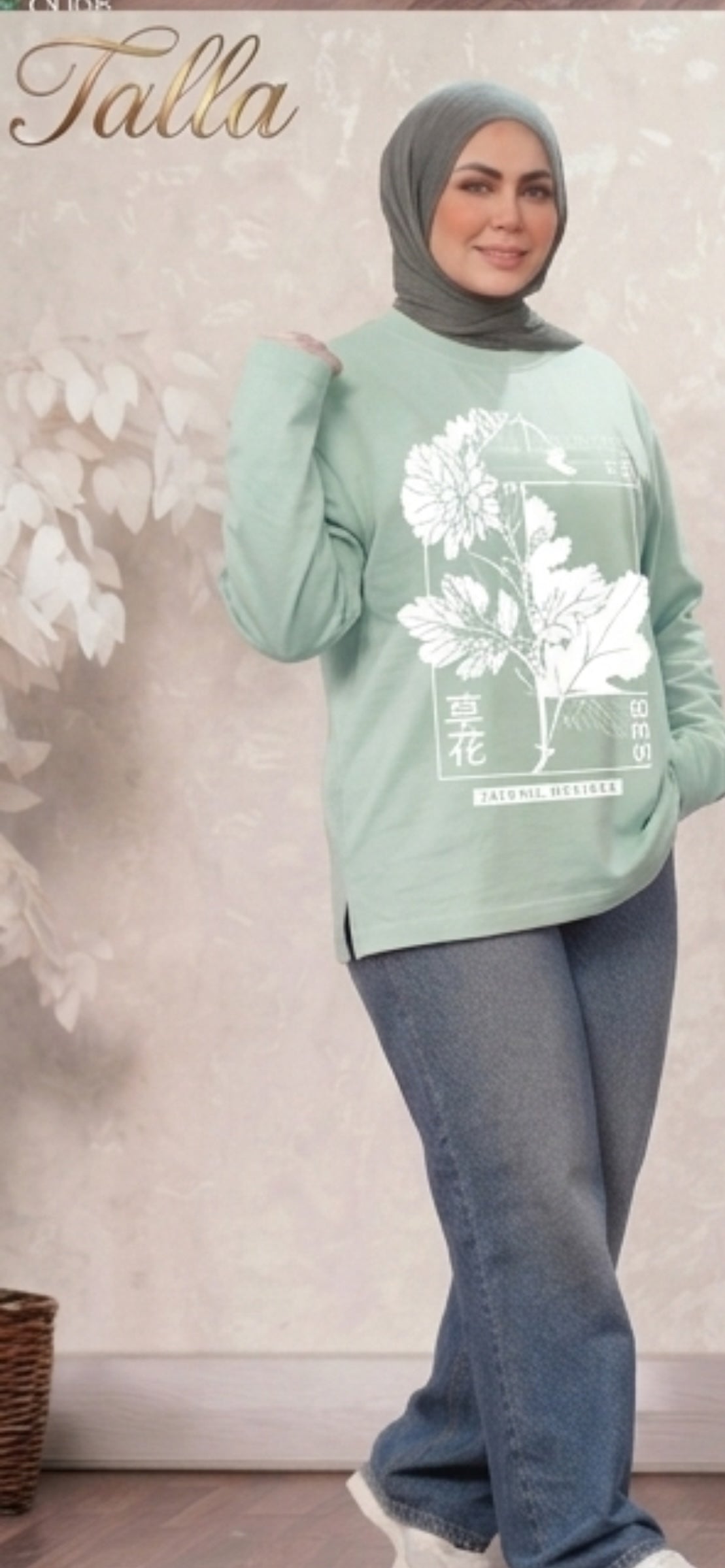 Model wearing a Talla | طلةّ sage green cotton top with a white floral graphic print and side slits with jeans
