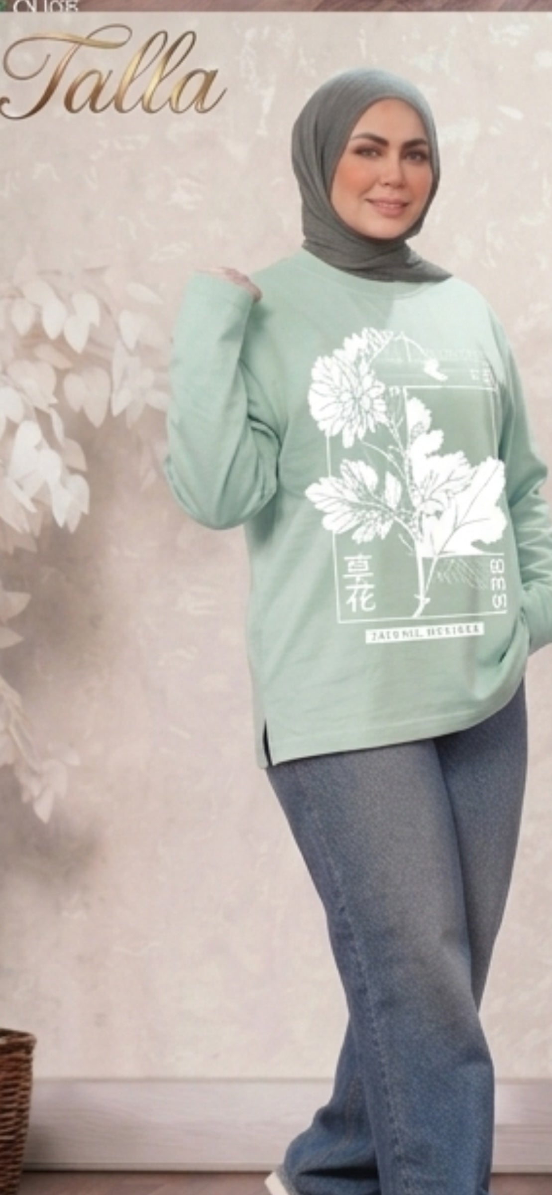 A woman wearing a Talla | طلةّ sage green long sleeve sweatshirt with a white floral graphic print and side slits.